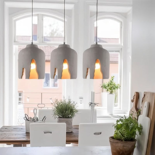 "Concrete pendant lights with sculptural design hanging over a wooden dining table, creating a modern industrial ambiance"