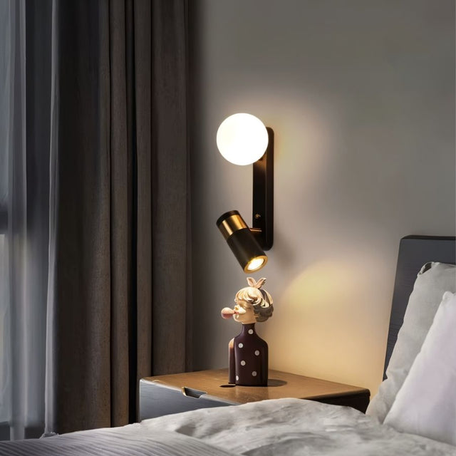 "A modern black bedside reading lamp with frosted glass globe and adjustable spotlight, mounted on a gray wall above a bedside table with a decorative figurine."