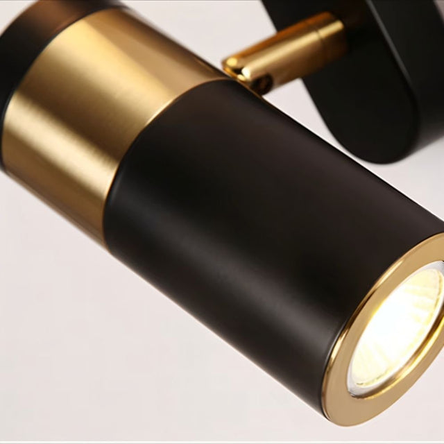 "Close-up of a modern black and gold bedside reading lamp with an adjustable cylindrical spotlight, showcasing the metallic joint and focused light."