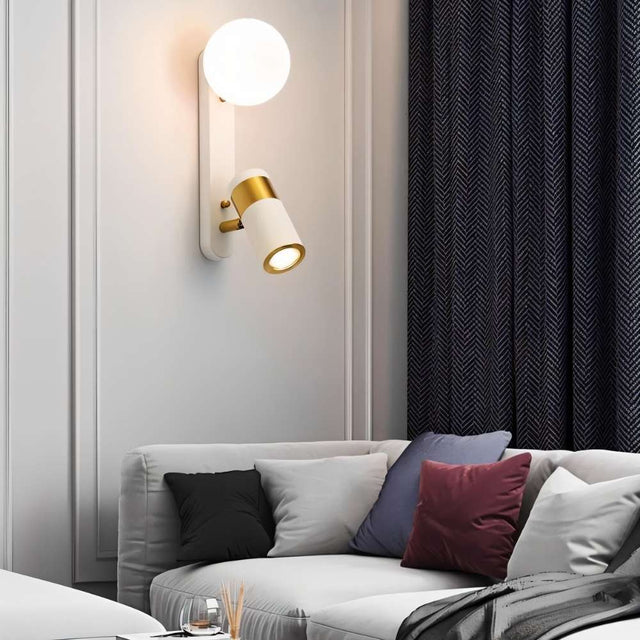 "A modern white bedside reading lamp with frosted glass globe and adjustable spotlight, mounted on a white wall in a living room with a gray sofa and dark blue curtains."