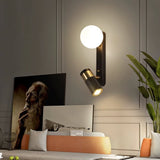 "A modern black bedside reading lamp with a frosted glass globe and adjustable spotlight, mounted on a white wall in a living room with contemporary art and plants."