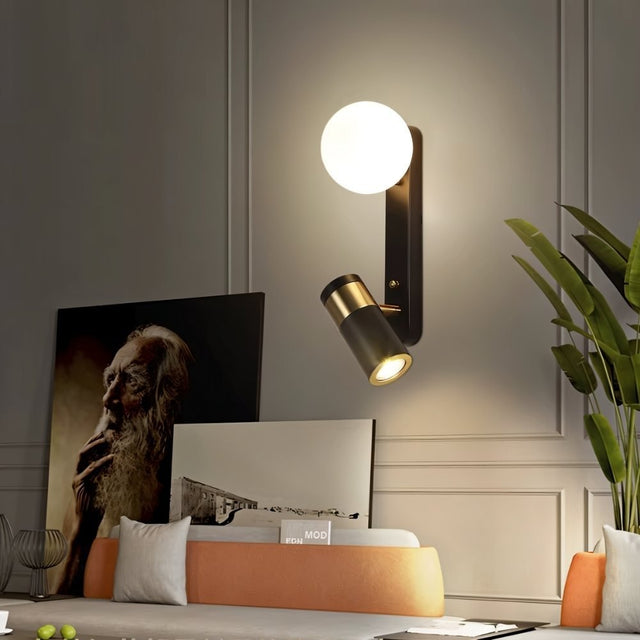 "A modern black bedside reading lamp with a frosted glass globe and adjustable spotlight, mounted on a white wall in a living room with contemporary art and plants."