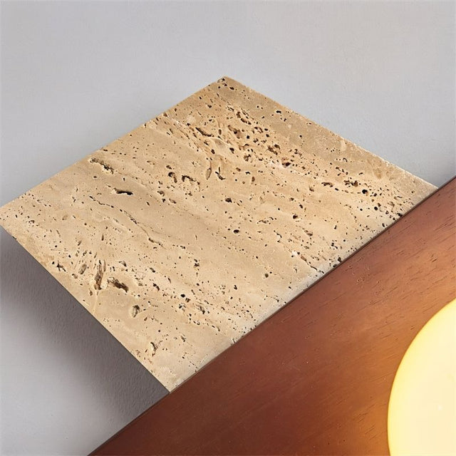 "Detailed close-up of the Eldis Wall Lamp, focusing on the warm diffused light it emits, framed by angular travertine and walnut."