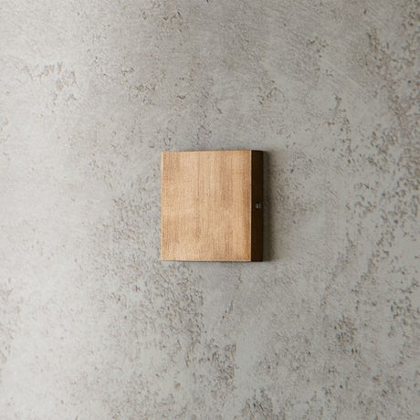 "modern square wall lamp, brass finish, minimalist design on textured wall"