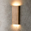 "brass wall lamp, vertical minimalist light, warm glow on textured wall"