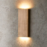 "brass wall lamp, vertical minimalist light, warm glow on textured wall"