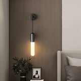 "A minimalist black wall lamp with a long, slender cylindrical shade casting a soft glow in a modern bedroom."