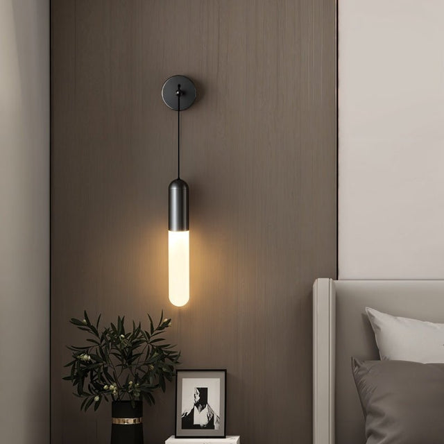 "A minimalist black wall lamp with a long, slender cylindrical shade casting a soft glow in a modern bedroom."