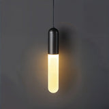 "A minimalist black pendant light with a long, slender cylindrical shade casting a soft, warm glow against a dark gray background."