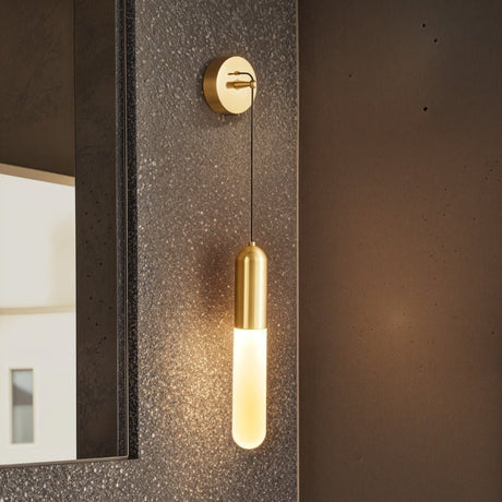 "A minimalist brass wall lamp with a long, slender cylindrical shade casting a soft glow on a textured wall in a modern bathroom."
