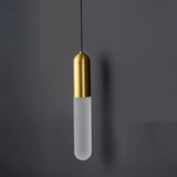 "A modern brass pendant light with a frosted, elongated cylindrical shade hanging against a dark gray background."