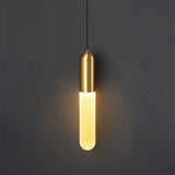 "A minimalist brass pendant light with a long, slender cylindrical shade casting a soft, warm glow against a dark gray background."