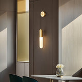 "A minimalist brass wall sconce with a long, slender cylindrical shade casting a soft glow on a dark wall in a modern living room."