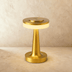 Modern cordless table lamp with brushed metal base and cream-colored circular shade on wooden desk with accessories.