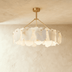Cloud-shaped pendant light with brass finish suspended over bedroom with gray upholstered headboard and blue accent wall.