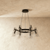 "A modern black brass linear chandelier with cone-shaped acrylic shades over a dining table."