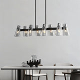 "A modern black brass linear chandelier with cone-shaped acrylic shades over a dining table."