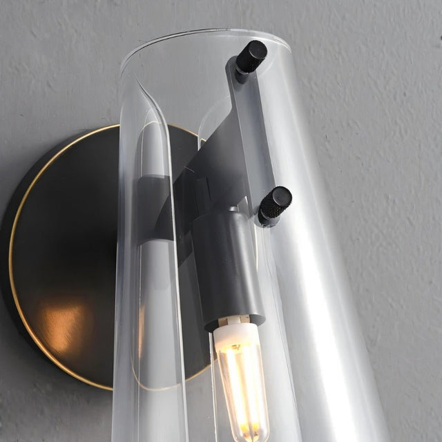 "Close-up of a modern brass wall lamp with a clear acrylic shade and exposed bulb."