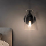 "A modern brass wall lamp with a clear acrylic shade, lit on a dark wall."