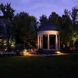 "Outdoor spotlights illuminating a garden gazebo at dusk."