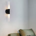 Black and frosted glass cylindrical wall sconce illuminating above a green upholstered armchair.