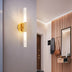 Modern wall sconce with cylindrical frosted glass shade and polished brass finish mounted in contemporary entryway.