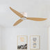 Three-blade ceiling fan with white motor housing and natural wood-finish blades mounted on white ceiling above framed wall art.