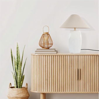 "Entola table lamp with a beige shade on a modern wooden cabinet with decorative items."