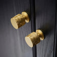 "Two gold textured Erdas knobs mounted on a dark wood cabinet."