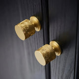 "Two gold textured Erdas knobs mounted on a dark wood cabinet."