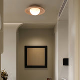 "A modern, minimalist flush mount light with a round travertine base and frosted globe, mounted on a hallway ceiling, providing a warm, ambient glow."
