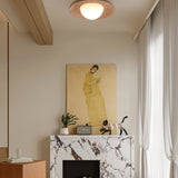 "Modern, minimalist flush mount light with a round travertine base and frosted globe, mounted on a living room ceiling above a fireplace with a marble mantelpiece and a painting."