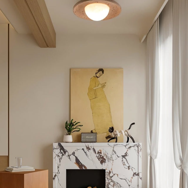 "Modern, minimalist flush mount light with a round travertine base and frosted globe, mounted on a living room ceiling above a fireplace with a marble mantelpiece and a painting."