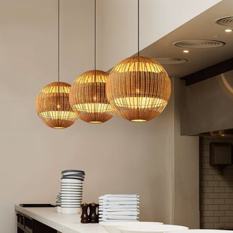 "Set of three handcrafted rattan pendant lights with spherical design and open weave, casting a warm, ambient glow. Ideal for kitchen decor, blending modern and natural aesthetics with durable rattan material."