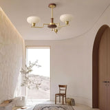 "Brass and wood chandelier with three white globe-shaped glass shades, hanging in a modern hallway with a chair and doorway."