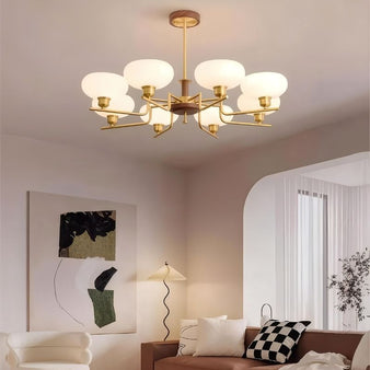 "Brass and wood chandelier with six white globe-shaped glass shades, hanging in a modern living room with abstract art and a sofa."