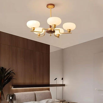 "Brass and wood chandelier with five white globe-shaped glass shades, hanging in a modern bedroom."