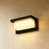 Black rectangular outdoor wall sconce with illuminated white panel on wooden slat facade at night.