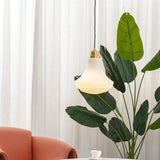 "Retro pendant light with a bell-shaped, striped glass shade and brass accents in a living room setting, casting a soft, inviting glow near a large indoor plant."