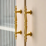 "Pair of ornate brass door handles with a classic design on a light-colored cabinet."