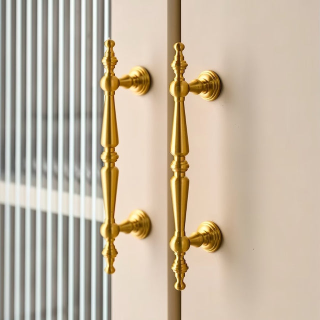 "Pair of ornate brass door handles with a classic design on a light-colored cabinet."