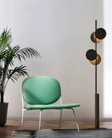 "A modern floor lamp with multiple circular shades, illuminating a living room with a green armchair and a houseplant."