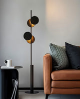 "A modern floor lamp with multiple circular shades, illuminating a living room with a leather sofa and side table."