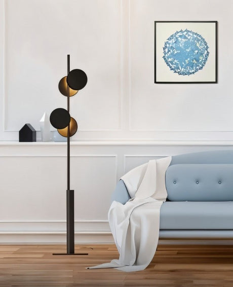 "A modern floor lamp with multiple circular shades, illuminating a living room with a blue sofa and artwork."