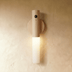 Wooden cylindrical table lamp with white opal glass shade on bedside table in modern bedroom setting.