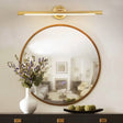 "A sleek gold wall lamp with a horizontal bar design, mounted above a round mirror in a contemporary bathroom setting."