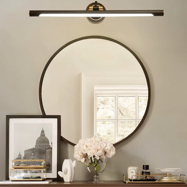 "A sleek black wall lamp with a horizontal bar design, mounted above a round mirror in a contemporary bathroom setting."