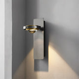 "A modern wall lamp with a single adjustable light, gunmetal finish, and glass lens, showing the light pattern on a gray wall."