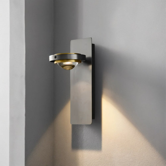 "A modern wall lamp with a single adjustable light, gunmetal finish, and glass lens, showing the light pattern on a gray wall."