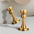 "Two brushed gold magnetic door stops, one standing upright and one tilted, against a blurred background."